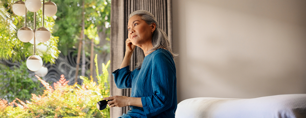 Image of female hearing aid wearer putting her hearing aids on beside a window